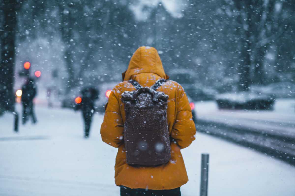 Ragazzo cammina nella neve con uno zaino in spalla al freddo e al gelo